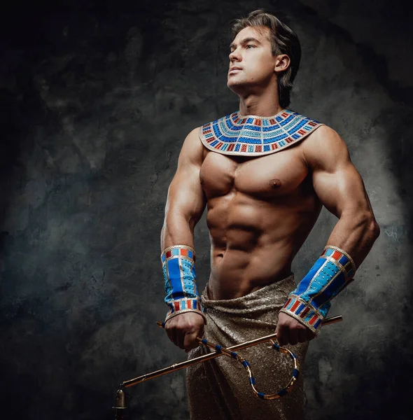 Atletisk man i en antik farao kostym på den mörka bakgrunden — Stockfoto