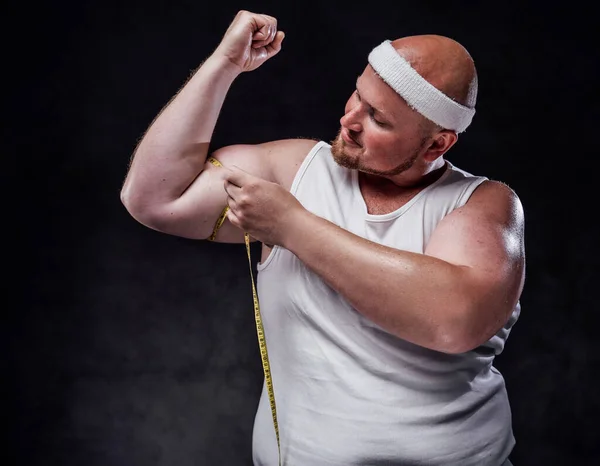 Hombre gordo en ropa deportiva mide su tamaño bíceps — Foto de Stock