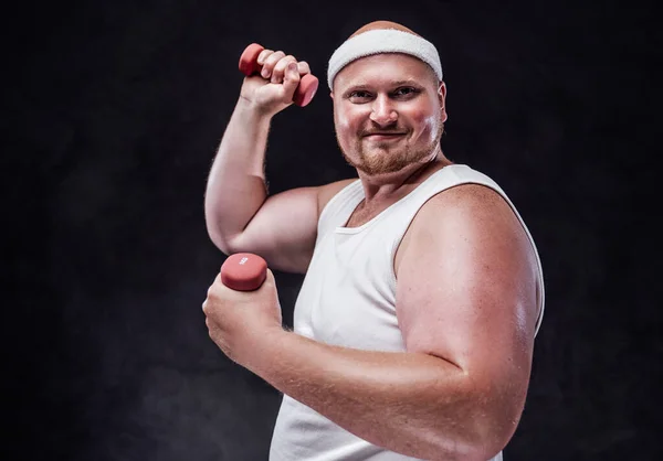 Un hombre gordo con un vendaje blanco en la cabeza levanta dos pesas rojas y mira a la cámara — Foto de Stock