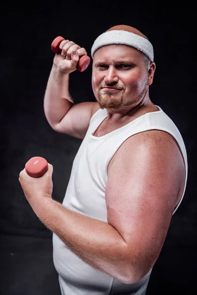 A plump man works out with two small dumbbells. The background is black — Stock Photo, Image