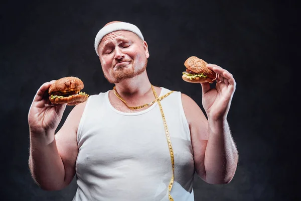 Sehr dicker Mann mit zwei Hamburgern in den Händen und geschlossenen Augen — Stockfoto