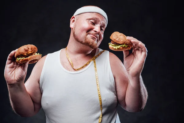 Fat man with two hamburgers in his hands and yellow tape measure around his neck