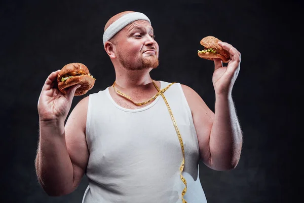 Смешной толстяк играет с двумя гамбургерами в руках — стоковое фото