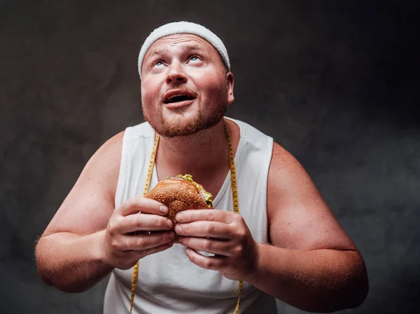 Bulky men with an open mouth looks on the light with a hamburger in his hands — Stock Photo, Image