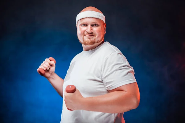 Um homem muito gordo em uma camiseta branca com dois halteres em cada mão — Fotografia de Stock