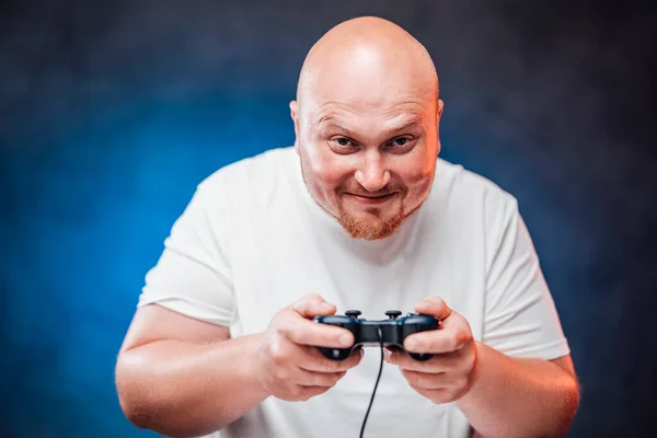 Hunky man in a white t-shirt plays a game console, smiling — Stock Photo, Image