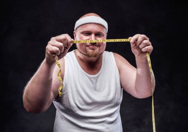 Gülümseyen şişman adam elindeki ölçü bandına bakıyor.