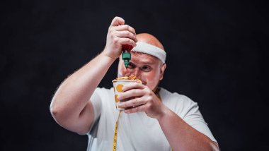 Spor kıyafetli şişman adam soslu patates kızartması yiyor.