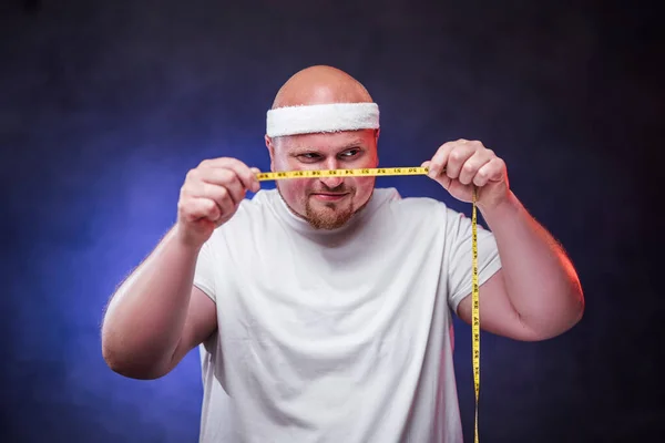 Nieuwsgierige dikke man goed kijkend naar de meetlint in zijn handen — Stockfoto