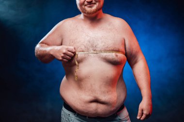 Gülümseyen şişman adam koca göbeğini gösteriyor ve göğüs kafesini ölçüyor.