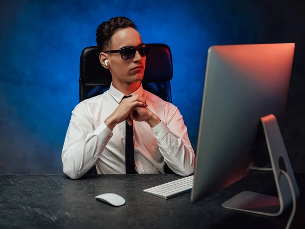A young office worker in in formalwear and sunglasses sits in the workplace — Stock Photo, Image