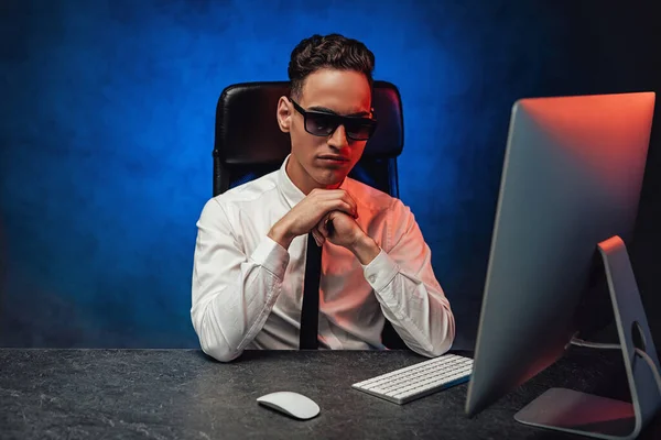 Serious young businessman in sunglasses working in office sitting at the workplace — Stock Photo, Image