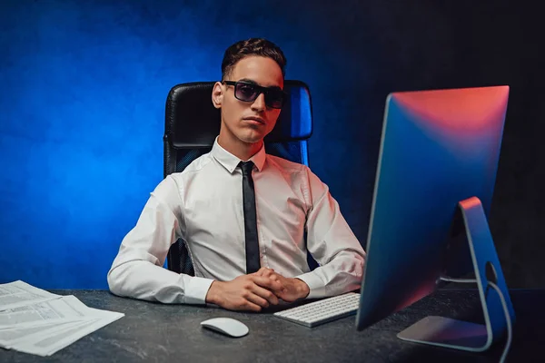 Confident young businessman in white shirt and sunglasses sitting at the office desk — Stock Photo, Image