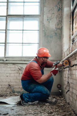 İnşaat alanında çekiçle tuğla bir duvarda çalışan şişkin bir inşaatçı.