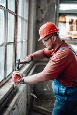 İnşaat alanındaki profesyonel inşaatçı çekiçle tuğla duvar üzerinde çalışıyor.