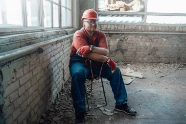 İnşaat alanının ortasında sandalyede oturan bir inşaatçı.