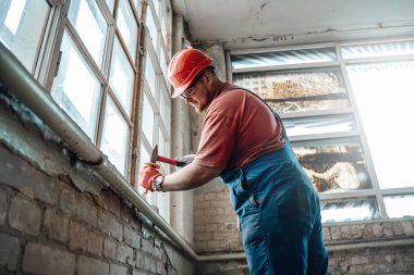 Bir inşaat alanında çekiçle pencere kenarında çalışan profesyonel bir inşaatçı.