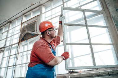 Büyük bir inşaat alanında penceresi olan şişman bir inşaatçı.