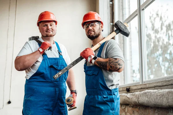 A couple of workers, holding a hammer and a sledgehammer