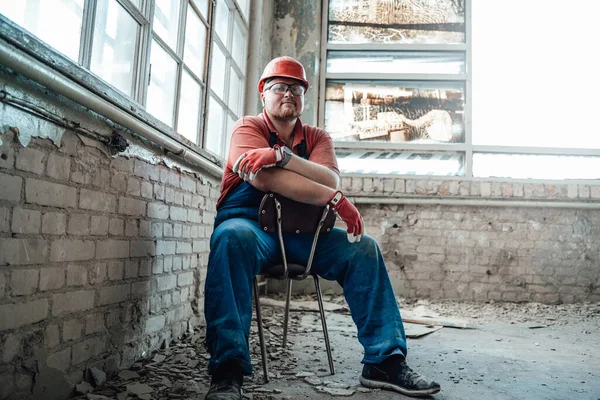 Tired worker sitting on a chair in the middle of a construction site — Stock Photo, Image