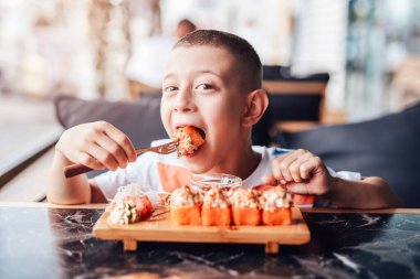 Çocuk açık kafede suşi yemeyi seviyor.