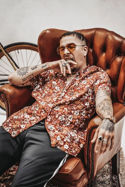 Tetovaný gangster zívá, zatímco sedí na luxusním retro křesle, vypadá velmi expresivně a šíleně — Stock fotografie