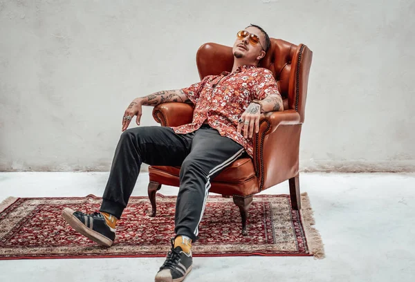 El tipo expresivo y elegante con camisa hawaiana y gafas de sol que se relaja en un sofá retro de lujo parece un gángster raro. — Foto de Stock