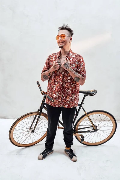 Tipo muy expresivo y elegante en gafas de sol y camisa hawaiana sosteniendo la bicicleta en su hombro — Foto de Stock