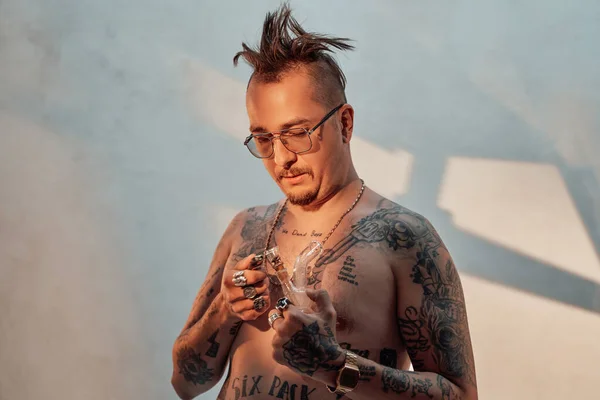 Hombre sin camisa con el cuerpo tatuado y corte de pelo raro sostiene la pipa con cannabis — Foto de Stock