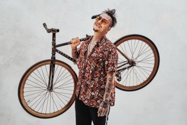 Güneş gözlüklü, Hawaii gömlekli, motosikleti omuzunda tutan çok etkileyici ve şık bir adam.