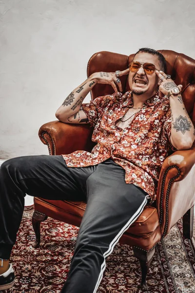 El tipo expresivo y elegante con camisa hawaiana y gafas de sol que se relaja en un sofá retro de lujo parece un gángster raro. — Foto de Stock
