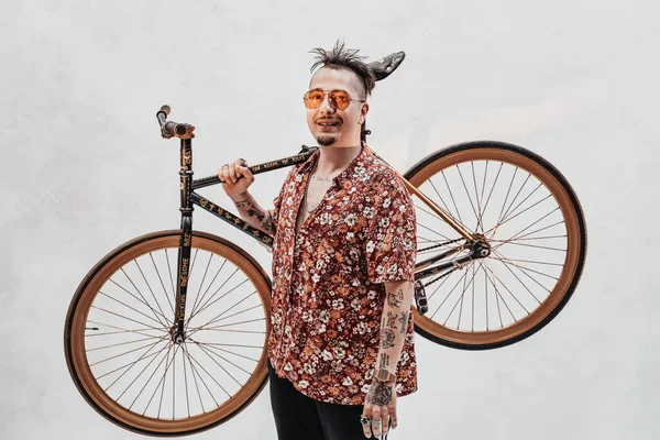 Nagyon kifejező és stílusos fickó napszemüvegben és hawaii ingben, aki a biciklit a vállán tartja. — Stock Fotó