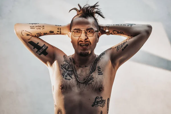 Elegante gángster en gafas con cuerpo desnudo tatuado y accesorios tomados de la mano detrás de su cabeza — Foto de Stock