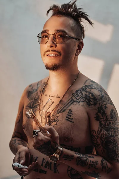 Hombre sin camisa con el cuerpo tatuado y corte de pelo raro sostiene la pipa con cannabis — Foto de Stock