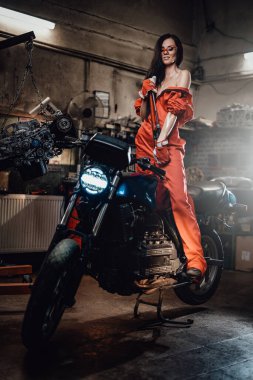 Motosiklette oturan genç seksi kadın, elinde büyük bir ingiliz anahtarı.