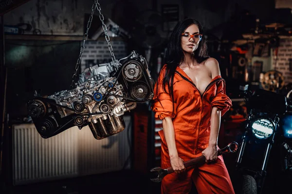 Sexy brunette in orange jumpsuit posing with a wrench in her hands — Stock Photo, Image