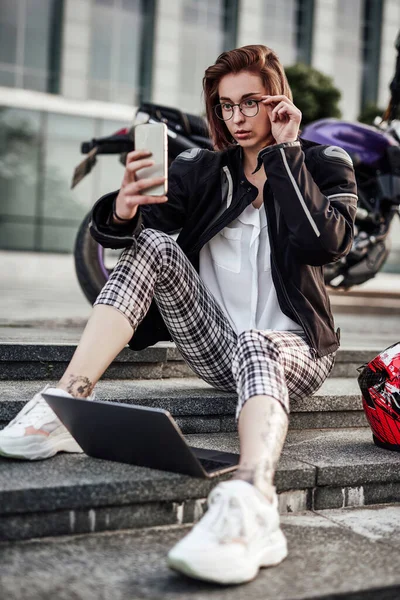 Sexy girl assis près de sa moto et regarde l'écran de son téléphone — Photo