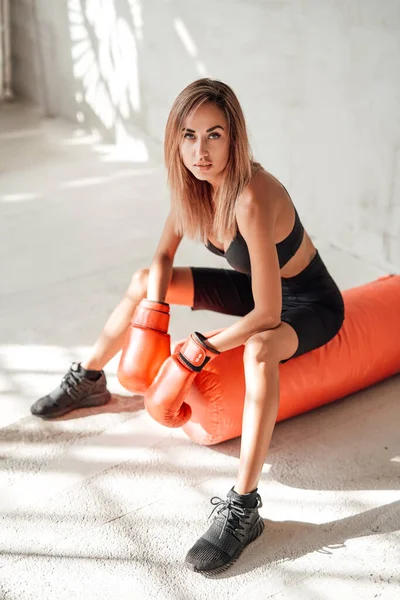 Sexy chica joven en un chándal negro con un saco de boxeo y guantes de boxeo — Foto de Stock