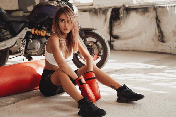 Sportive sexy posant dans un studio assis sur le sol avec un sac de boxe. — Photo