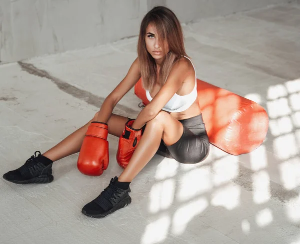 Mujer deportiva peligrosa y sexy posando en un estudio sentado con un saco de boxeo. —  Fotos de Stock