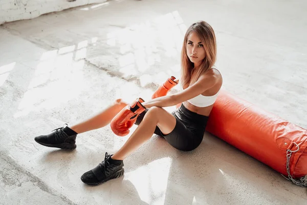 Atractiva deportista sentada en el suelo con un saco de boxeo. — Foto de Stock