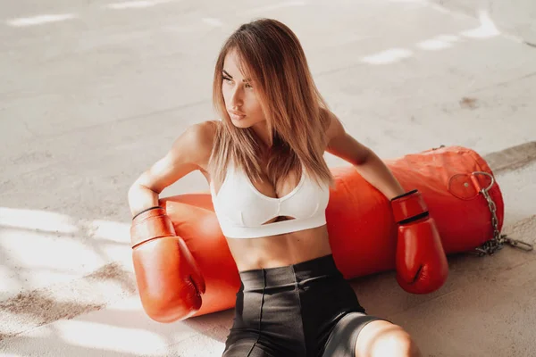 Deportiva caliente sentada en el suelo con un saco de boxeo. —  Fotos de Stock