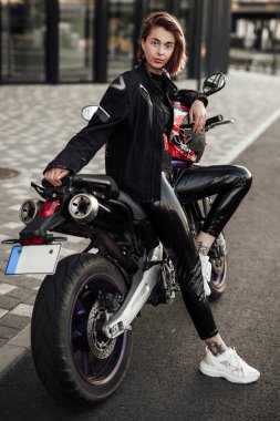 Siyah ceketli seksi kadın kırmızı kasklı mor bir motosikletin üzerinde oturuyor.