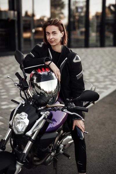 Χαμογελαστό κορίτσι σε ένα μπουφάν μοτοσικλέτας κάθεται με ένα κράνος μοτοσικλέτας σε μια μοτοσικλέτα — Φωτογραφία Αρχείου