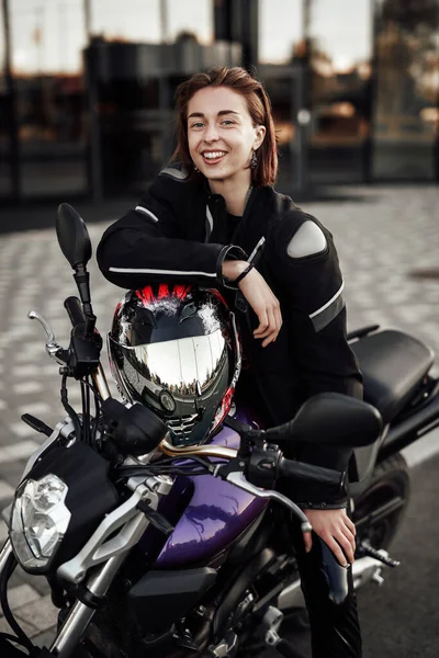 Ευτυχισμένο κορίτσι σε ένα μπουφάν μοτοσικλέτας κάθεται με ένα κράνος μοτοσικλέτας σε μια μοτοσικλέτα — Φωτογραφία Αρχείου