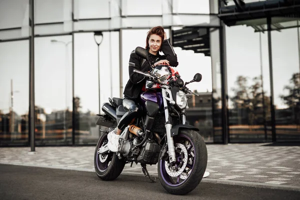 Χαριτωμένο κορίτσι σε ένα μπουφάν μοτοσικλέτας κάθεται με ένα κράνος μοτοσικλέτας σε μια μοτοσικλέτα — Φωτογραφία Αρχείου