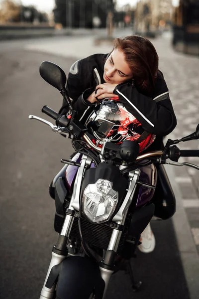 Χαριτωμένο κορίτσι σε ένα μπουφάν μοτοσικλέτας κάθεται με ένα κράνος μοτοσικλέτας σε μια μοτοσικλέτα — Φωτογραφία Αρχείου