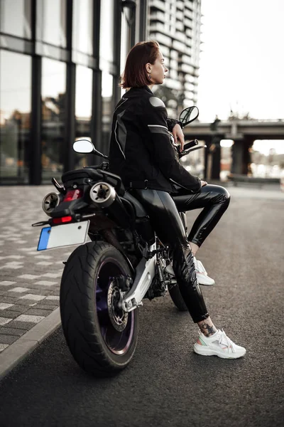 오토바이 재킷을 입은 멋진 소녀가 오토바이 헬멧을 쓴 채 오토바이에 앉아 있다 — 스톡 사진