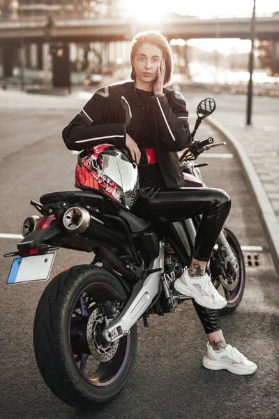 Bella ragazza in giacca si siede su una moto viola con un casco di sicurezza rosso e nero — Foto Stock