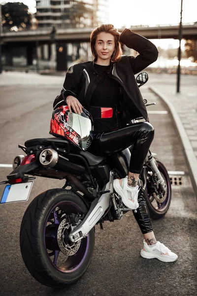 Lächelndes Mädchen in schwarzer Jacke sitzt auf einem lila Motorrad mit Schutzhelm — Stockfoto